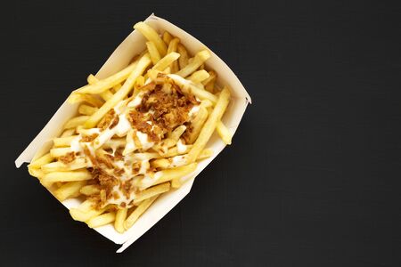 French fries with cheese sauce and onion in a paper box on a black background, top view. Flat lay, overhead, top view. Copy space.の写真素材