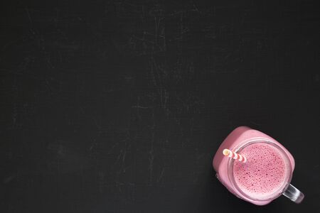 Mason glass jar mug filled with raspberry smoothie on a black background, top view. Flat lay, overhead, from above. Copy space.の写真素材