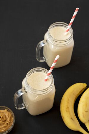 Mason glass jar mugs filled with peanut butter banana smoothie on a black background, low angle view. Copy space.の写真素材