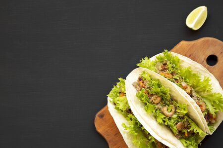 Shrimp tacos on a rustic wooden board on a black background, top view. Mexican cuisine. Flat lay,...