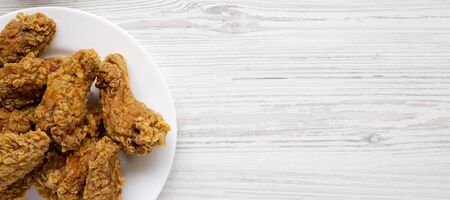 Chicken wings on a round white plate on a white wooden background. Overhead, flat lay, from above. Copy space.の写真素材