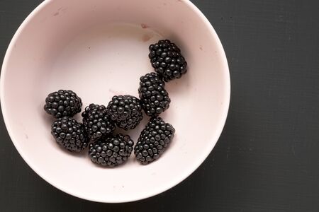 Blackberries in a pink bowl on a black background, top view. Summer berry.