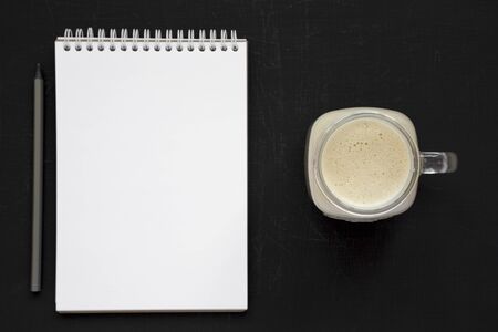 Peanut butter banana smoothie in a glass jar, blank notepad on a black background, overhead view. From above, flat lay, top view.の写真素材
