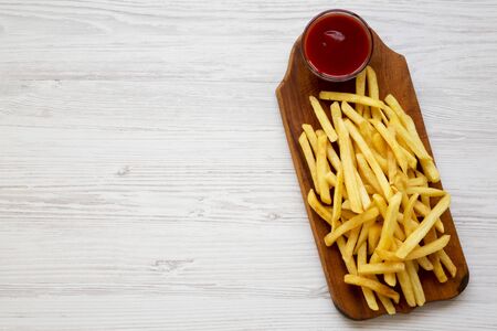 French fries with sauce on a rustic wooden board on a white wooden surface, top view. From above,...