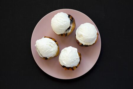 Homemade grilled peaches with vanilla ice cream on a pink plate on a black background, top view....