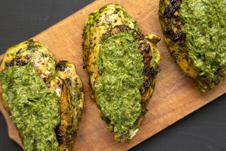 Grilled chimichurri chicken breast on a rustic wooden board on a black background, top view. Flat lay, overhead, from above. Close-up.の写真素材
