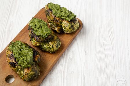 Grilled chimichurri chicken breast on a rustic wooden board on a white wooden background, low angle view. Space for text.の写真素材