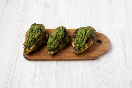 Grilled chimichurri chicken breast on a rustic wooden board on a white wooden surface, low angle view.の写真素材