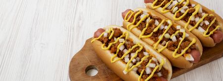 Homemade detroit style chili dog on a rustic wooden board on a white wooden table, side view. Space for text.の写真素材