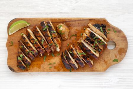 Grilled chipotle chicken breast on a rustic wooden board on a white wooden surface, top view. Flat...