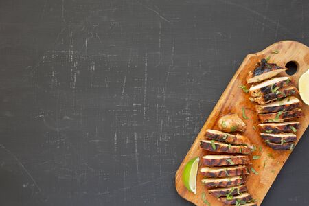 Grilled chipotle chicken breast on a rustic wooden board on a black surface, top view. Flat lay, overhead, from above. Copy space.の写真素材