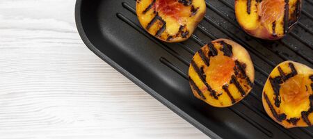 Homemade grilled peaches in a grilling pan on a white wooden surface, top view. Flat lay, overhead, from above. Space for text.の写真素材