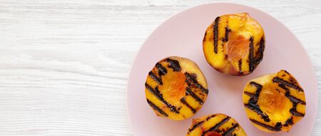 Homemade grilled peaches on a pink plate on a white wooden surface, top view. Flat lay, overhead, from above. Space for text.の写真素材