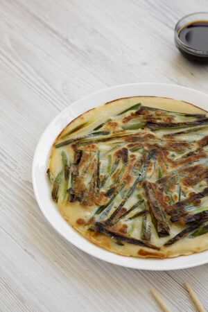 Homemade korean Pajeon scallion pancake on a white plate on a white wooden surface, side view. Asian food. Copy space.の写真素材