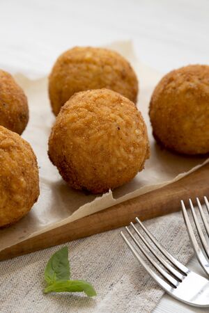 Homemade fried Arancini with basil on a rustic wooden board, side view. Italian rice balls....