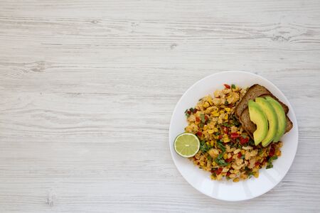 Homemade southwestern egg scramble with toast on a white plate on a white wooden background. Flat...