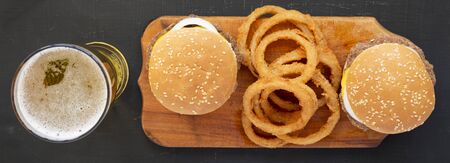 Homemade Mississippi Slug Burgers with onion rings on a rustic wooden board on a black surface, top...