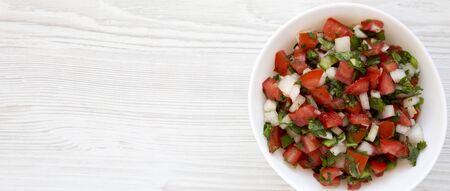 Pico de Gallo in a white bowl on a white wooden surface, top view. Overhead, from above, flat lay. Space for text.の写真素材