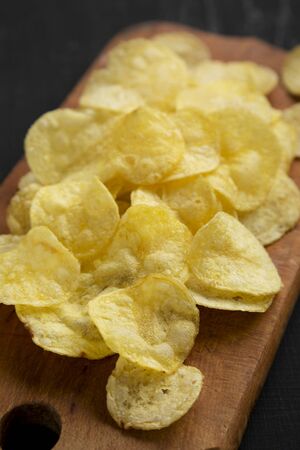 Crispy potato chips with salt on a rustic wooden board on a black surface, side view. Closeup.の写真素材