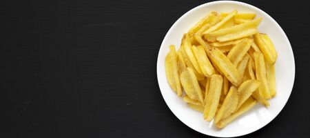 Homemade french fries on a white plate on a black background, top view. Flat lay, overhead, from above. Copy space.の写真素材