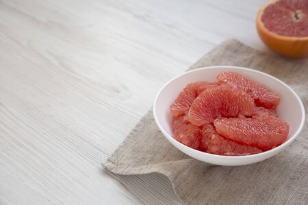 Red grapefruit slices in a white bowl on a white wooden background, side view. Copy space.の写真素材