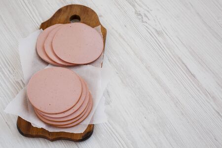 Sliced pork bologna meat on a rustic wooden board on a white wooden background, low angle view. Copy...