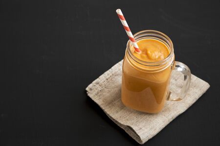 Homemade pumpkin smoothie in a glass jar mug over black background, low angle view. Copy space.の写真素材