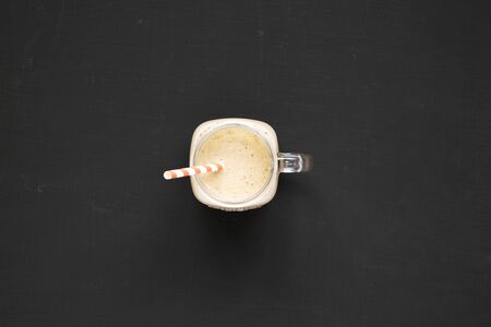 Glass jar mug filled with coffee, oat and banana smoothie on a black surface, overhead view. Top view, from above, flat lay. の写真素材