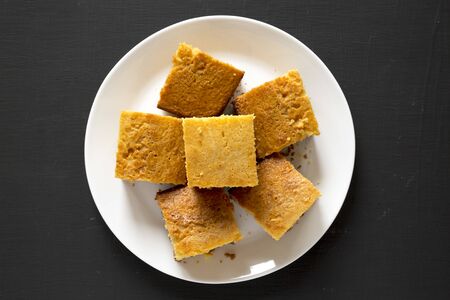 Homemade Sliced Cornbread Ready to Eat on a white plate on a black surface, top view. Flat lay,...