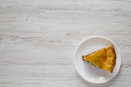 Slice of Homemade Canadian Tourtiere meat pie on a white plate over white wooden surface, top view....