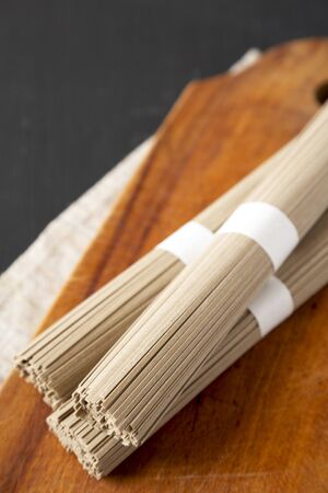 Uncooked Buckwheat Soba Noodles on a rustic wooden board on a black background, low angle view. Copy...