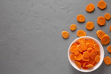 Overhead view, Fresh Raw Organic Carrot Chips in a white bowl over gray surface. From above,...