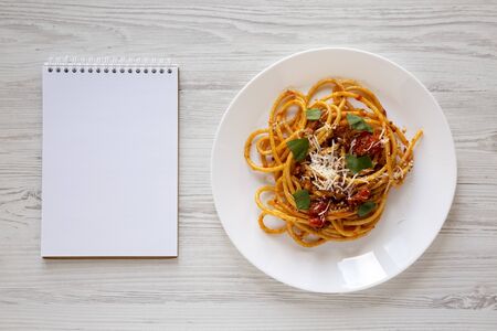 Homemade Bucatini all Amatriciana Pasta in a plate, blank notepad on a white wooden table, top view....