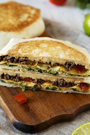 Tasty Homemade Beef Crunchwrap Quesadilla on a rustic wooden board, low angle view.の写真素材