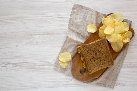 Homemade Peanut Butter Pickle Sandwich with Potato Chips on a rustic wooden board on a white wooden surface, top view. Flat lay, overhead, from above. Copy space.の写真素材