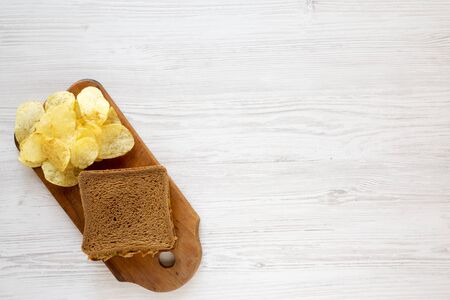 Homemade Peanut Butter Pickle Sandwich with Potato Chips on a rustic wooden board on a white wooden...
