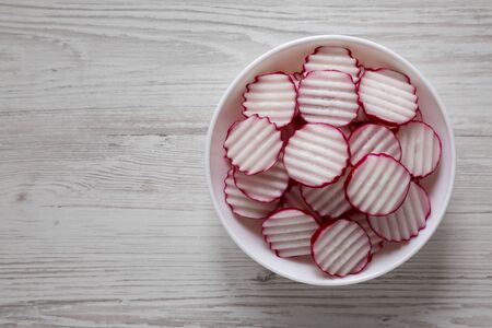 Radish Chips Slices in a white bowl on a white wooden surface, top view. Flat lay, overhead, from above. Copy space.の写真素材