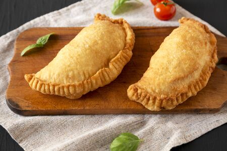Homemade Deep Fried Italian Panzerotti Calzone on a rustic wooden board on a black surface, low angle view. Close-up.の写真素材
