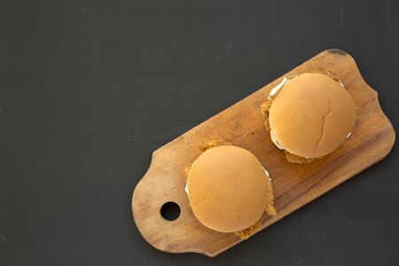 Homemade Burgers with fried chicken strips on a rustic wooden board on a black surface, top view....