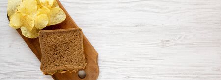 Homemade Peanut Butter Pickle Sandwich with Potato Chips on a rustic wooden board on a white wooden...