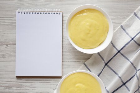 Homemade vanilla custard pudding in white bowls, blank notepad, top view. Flat lay, overhead, from above. Space for text.の写真素材