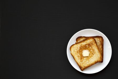 Homemade Buttered Toast on a white plate on a black background, top view. Flat lay, overhead, from above. Copy space.の写真素材