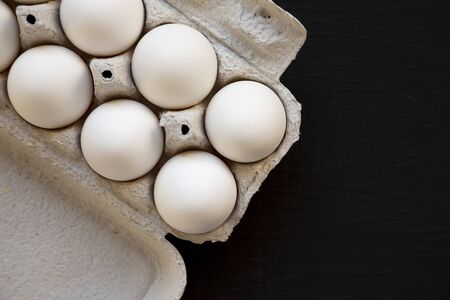 Uncooked Organic White Eggs in a paper box on a black surface, top view. Flat lay, overhead, from...