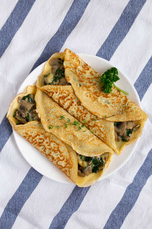 Savory Homemade Mushroom, Spinach and Cheese Crepes on a white plate on cloth, top view. Flat lay,...