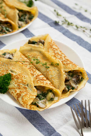 Savory Homemade Mushroom, Spinach and Cheese Crepes on a white plate on cloth, side view.