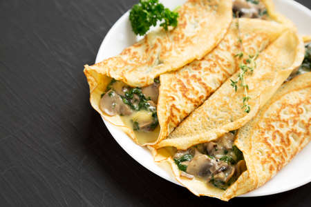 Savory Homemade Mushroom, Spinach and Cheese Crepes on a white plate on a black background, side...