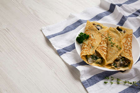 Savory Homemade Mushroom, Spinach and Cheese Crepes on a white plate on cloth, low angle view. Copy space.の写真素材