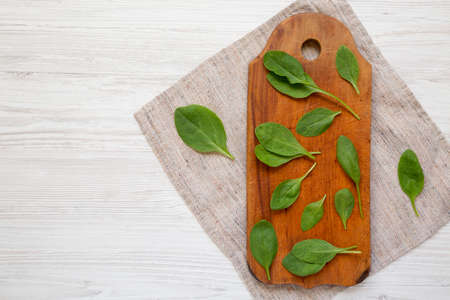 Fresh Baby Spinach on a rustic wooden board on a white wooden table, top view. Overhead, from above,...