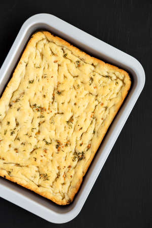 Home-baked Rosemary Garlic Focaccia Bread on baking tray on black background, top view. Flat lay,...
