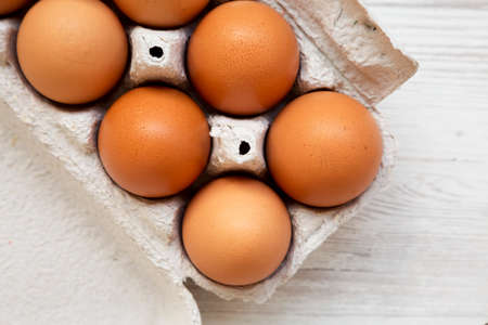 Raw Brown Eggs in a paper box on a white wooden background, top view. Flat lay, overhead, from...